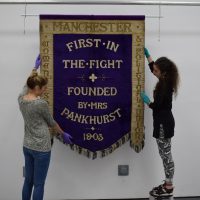 PHM's conservation team (Jenny van Enckevort & Kloe Rumsey) with the Manchester suffragette banner - image courtesy of People's History Museum