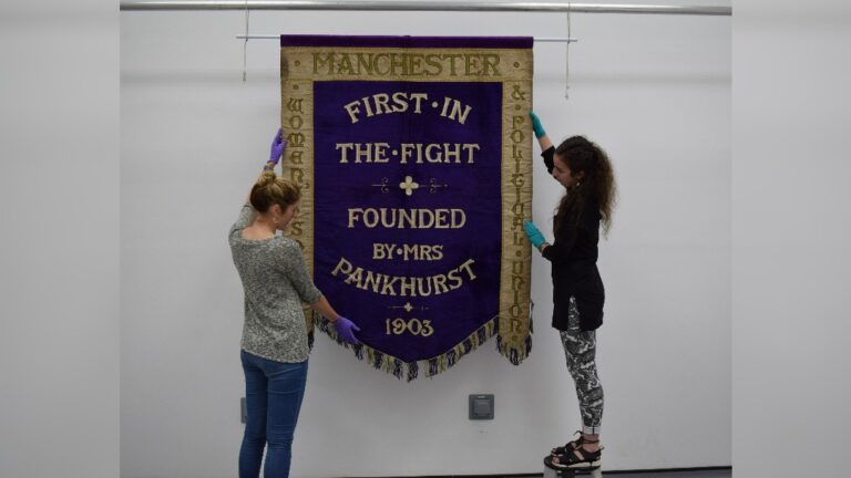 PHM's conservation team (Jenny van Enckevort & Kloe Rumsey) with the Manchester suffragette banner - image courtesy of People's History Museum