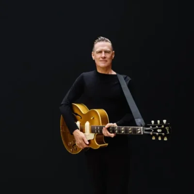 promotional image of Bryan Adams holding a guitar