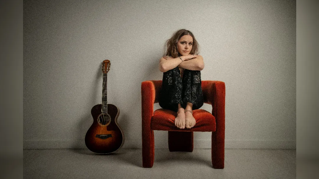 image of Taylor Rae sat on a chair next to her guitar. image courtesy Barbara FG